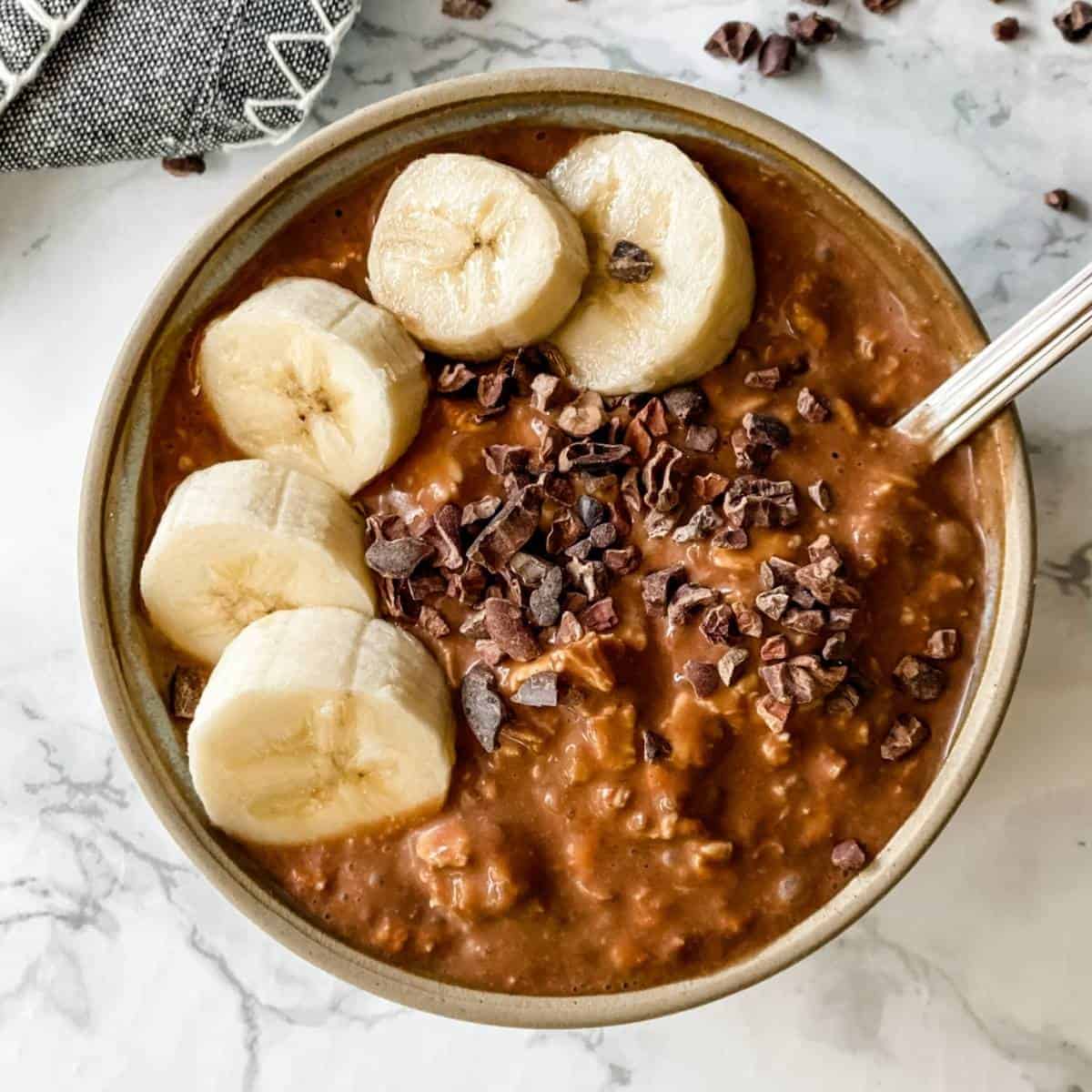 Chocolate Banana Overnight Oats in a bowl with bananas and chocolate nibs.