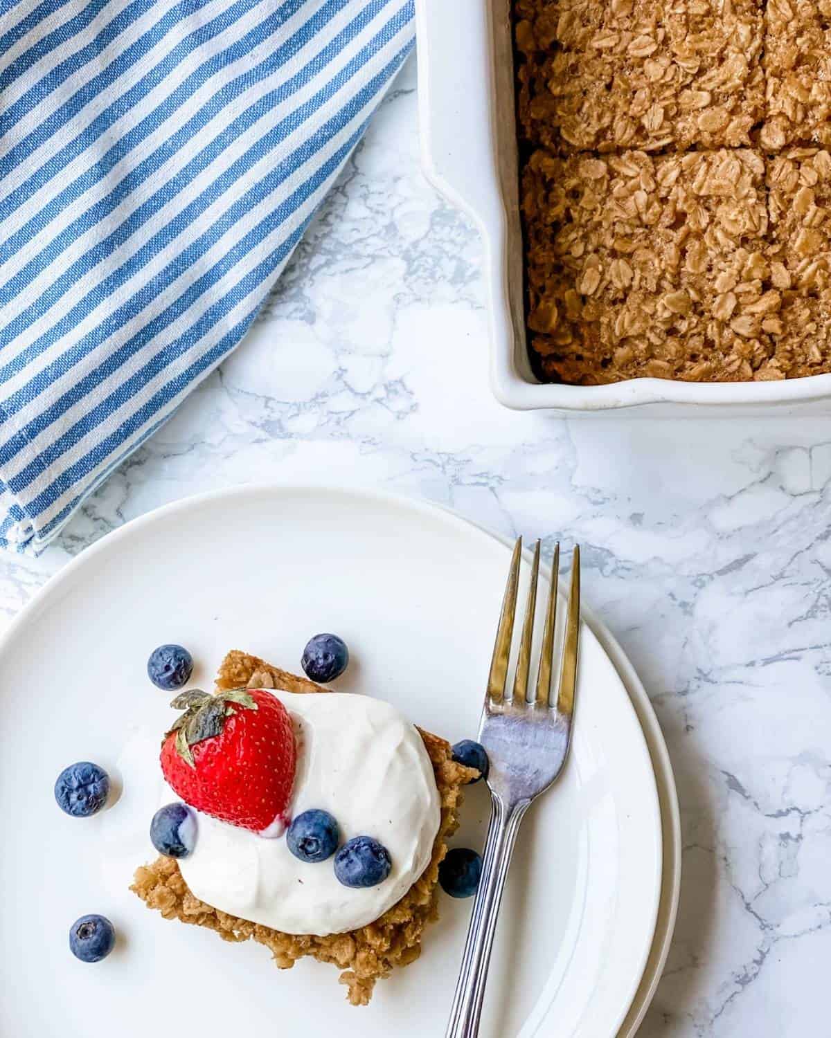 baked oatmeal on dish with the pan of oatmeal next to it.