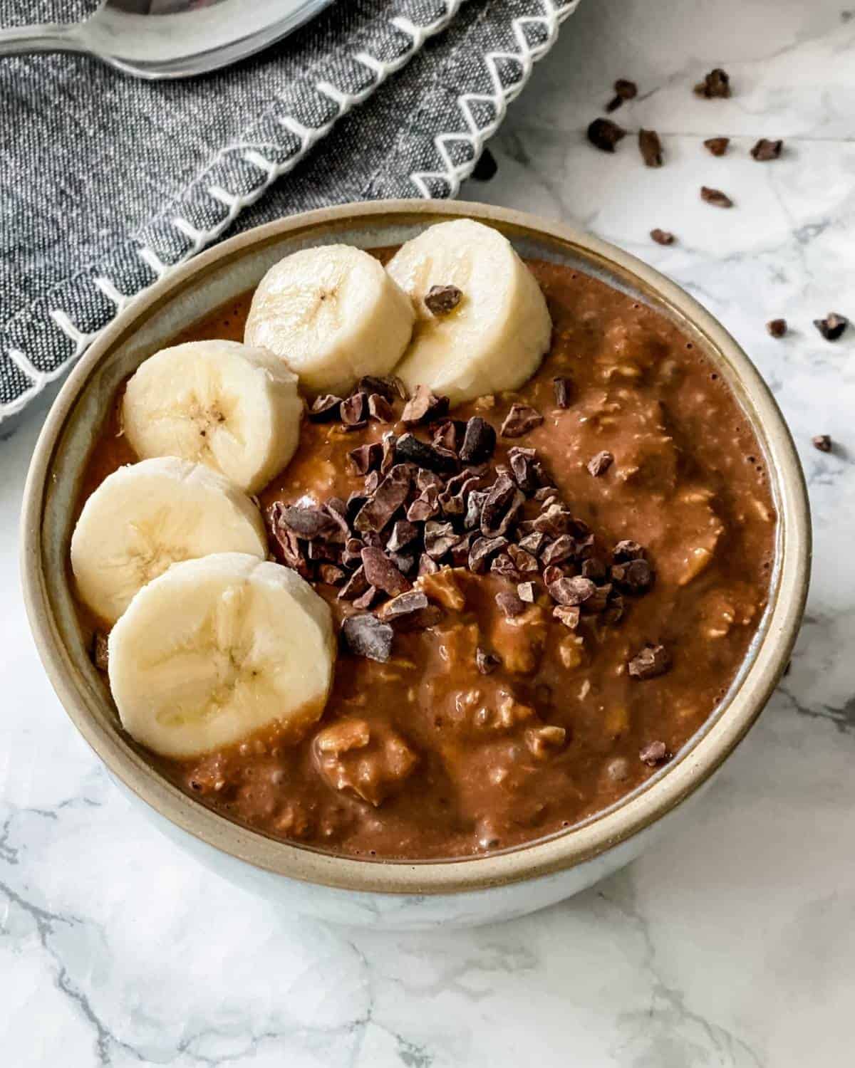 A bowl of creamy overnight oats with banana and cacao nibs on top.