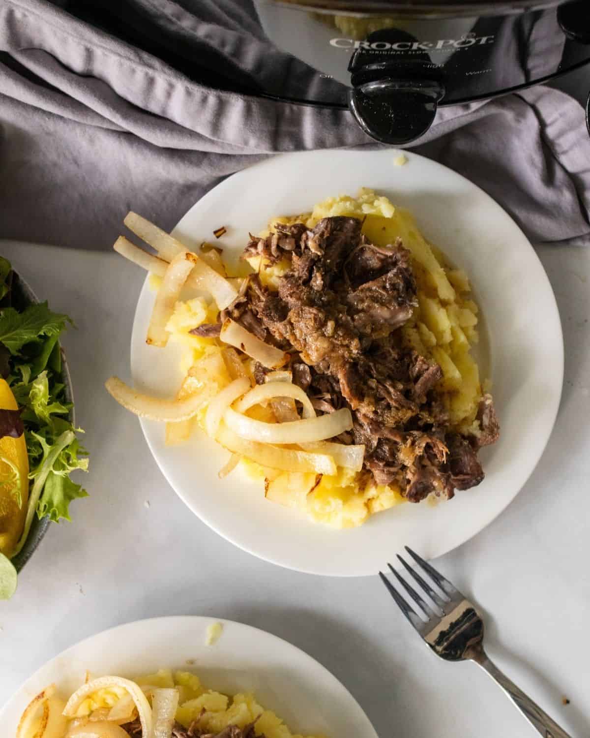 crockpot pot roast on plate with mashed potatoes and onions