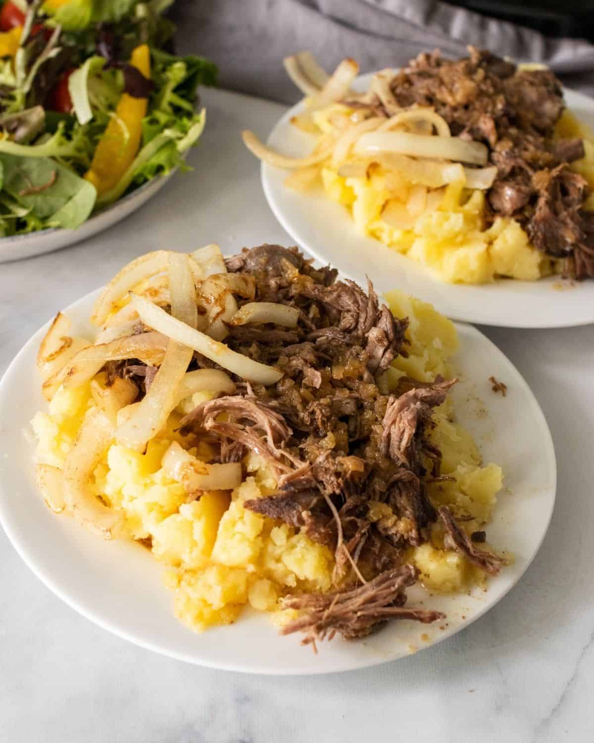 Plates of mashed potatoes and crockpot pot roast with a side salad