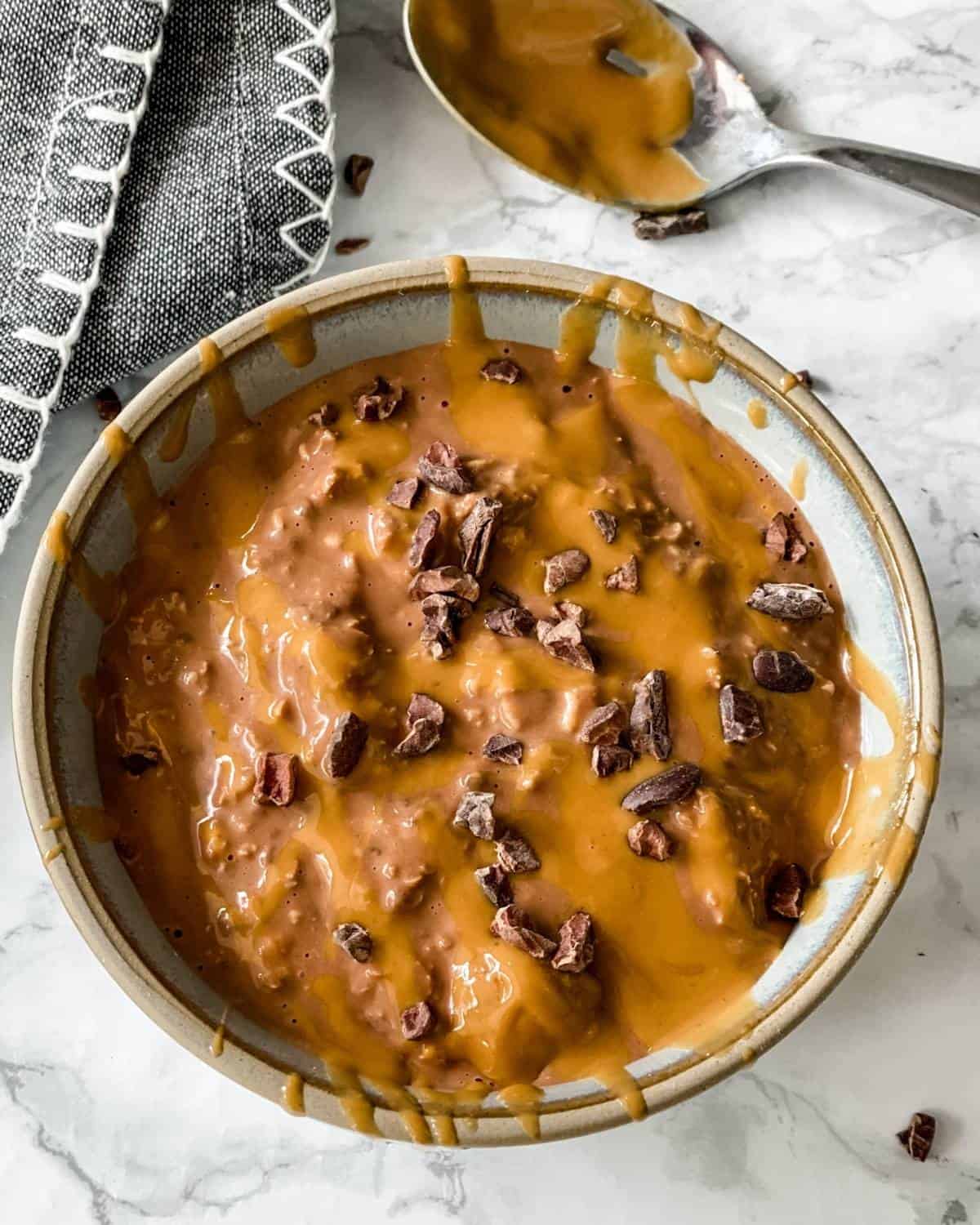 a bowl of creamy chocolate overnight oats with peanut butter drizzled on top and sprinkled with cacao nibs