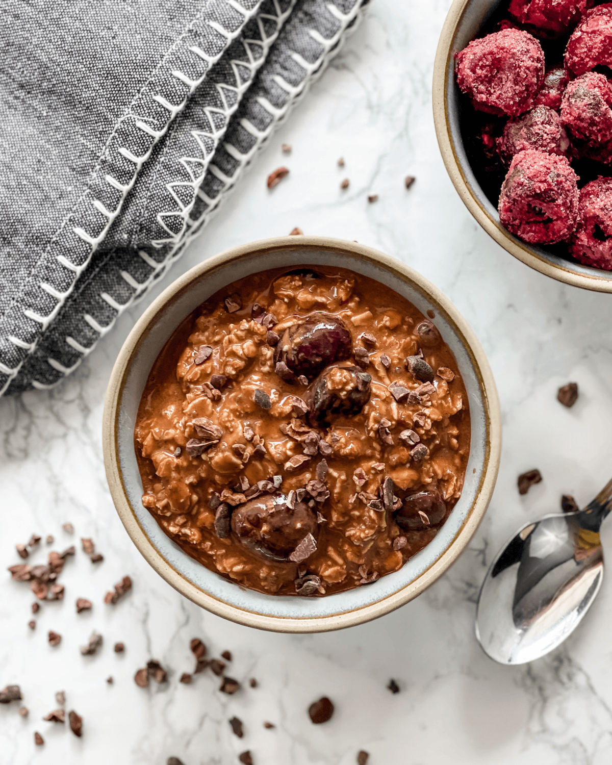 overhead picture of black forrest overnight oats in a bowl with a side bowl of frozen cherries.