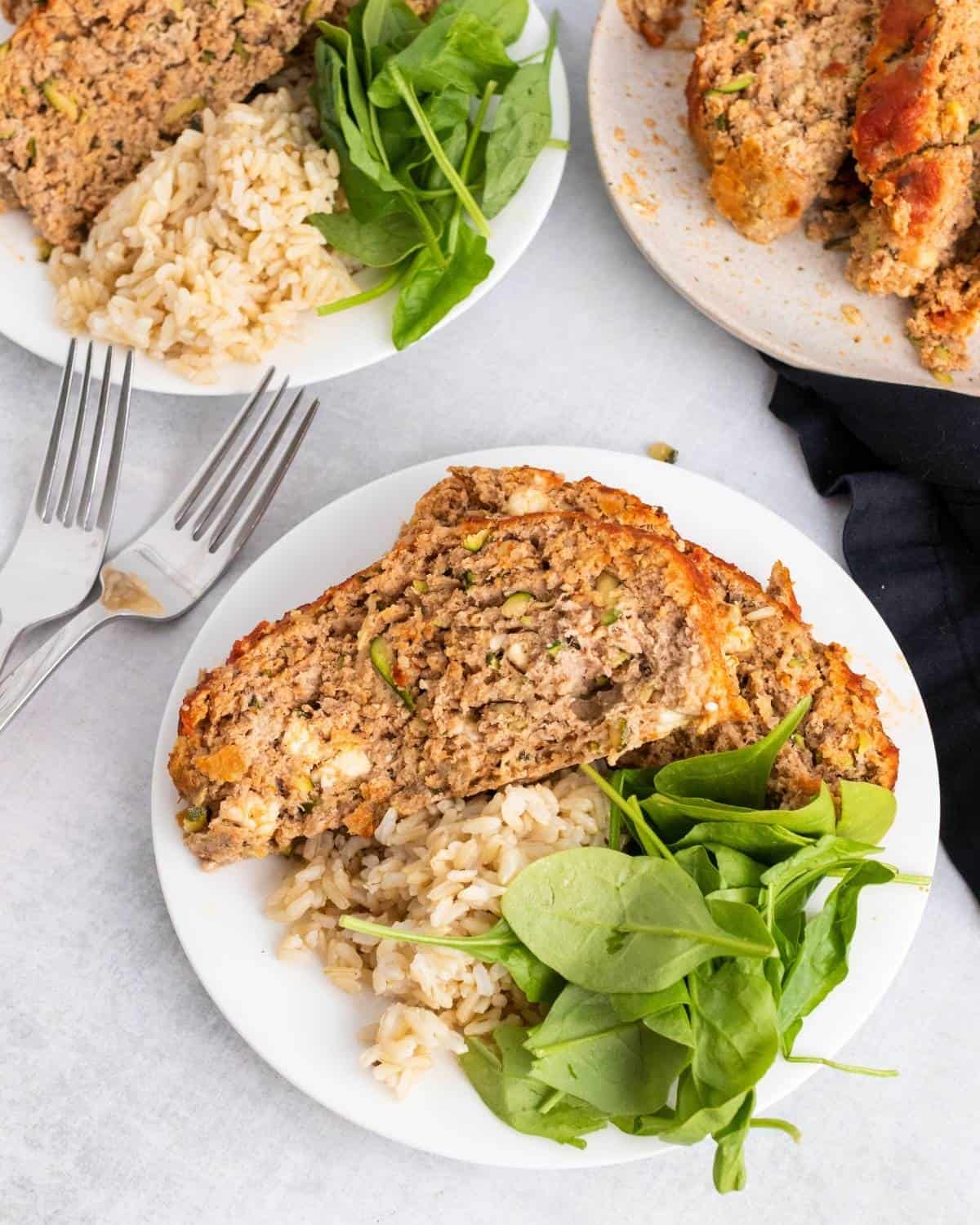 Turkey meatloaf with zucchini and feta on a plate with rice and baby spinach