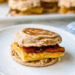 Close-up picture or egg, bacon and cheese breakfast sandwich on a white plate.