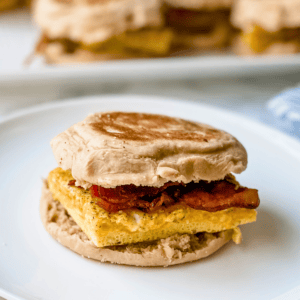 Close-up picture or egg, bacon and cheese breakfast sandwich on a white plate.