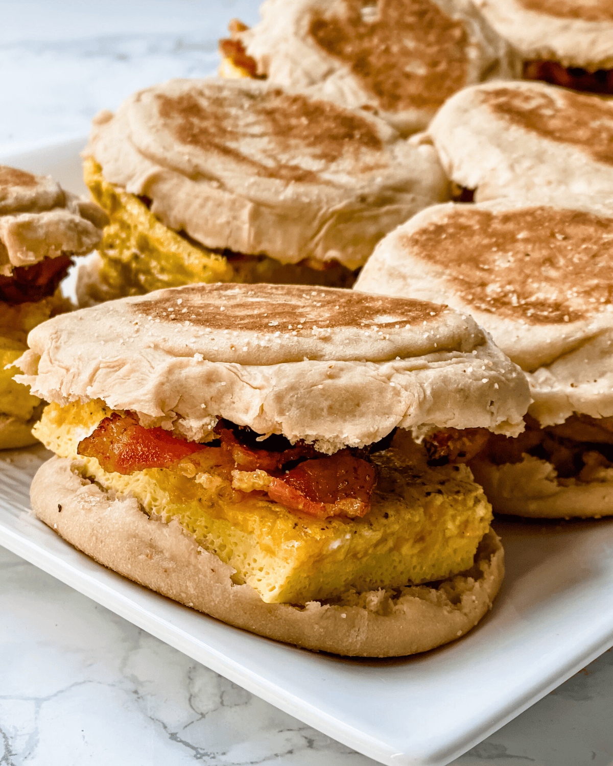 egg, bacon, and cheese breakfast sandwiches on a white platter.