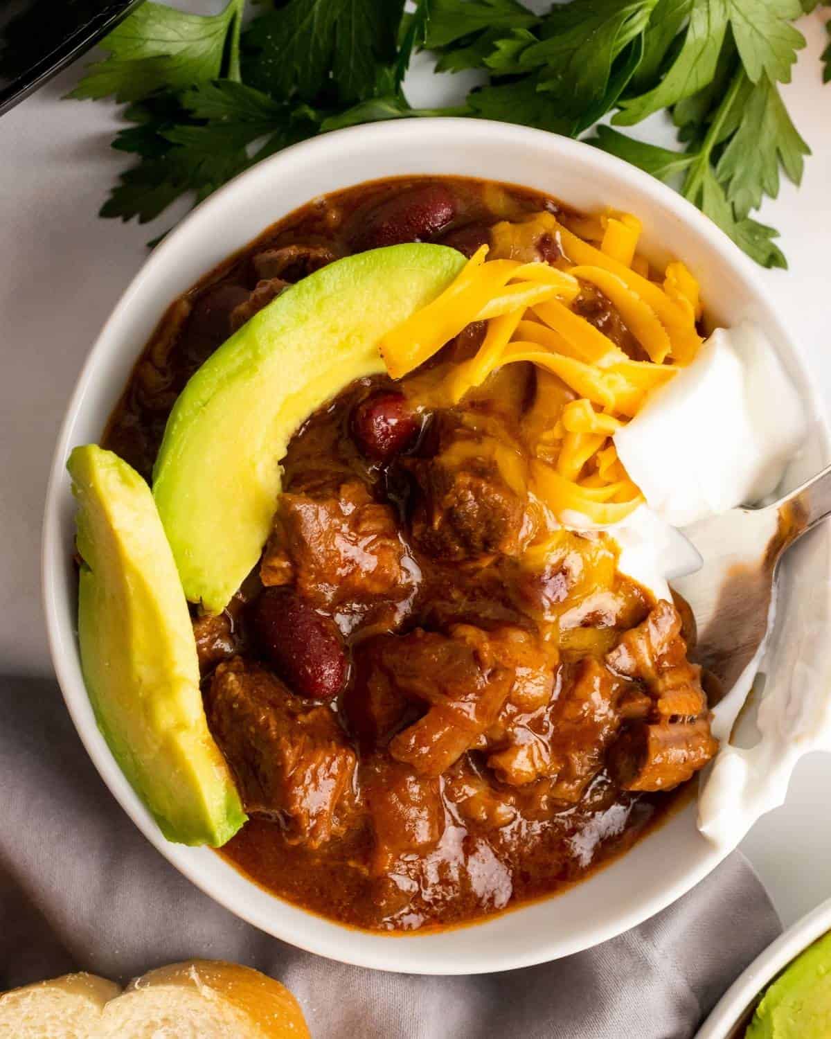 overhead shot of chunky beef chili with sliced avocado, cheese, and onion.