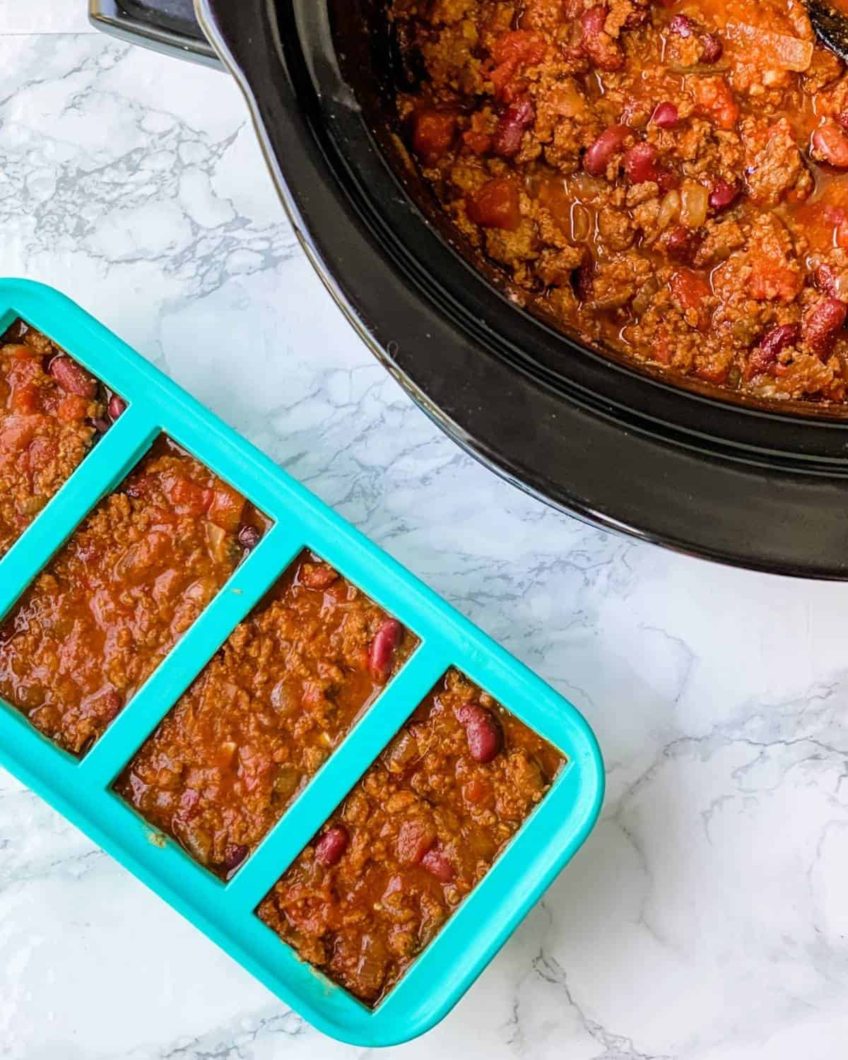 silicone souper cube trays with chili next to a slow cooker of chili