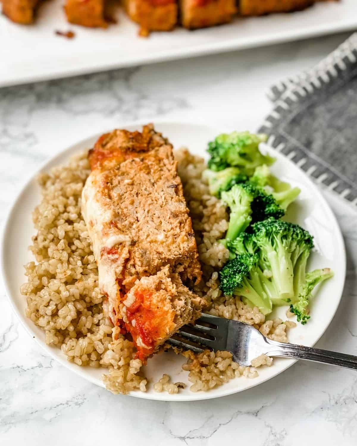 a slice of Italian meatloaf on a plate with rice and broccoli.