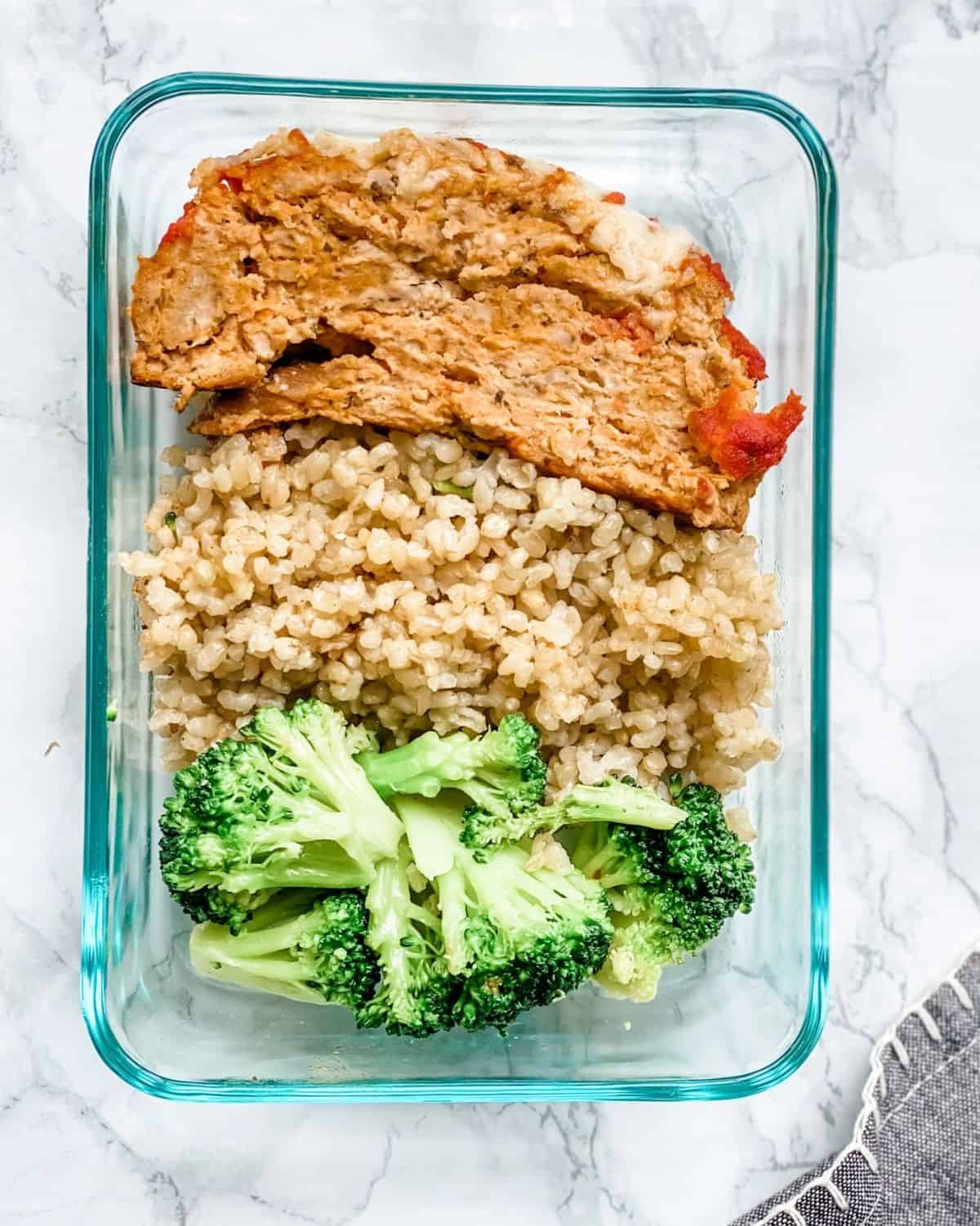 Italian meatloaf in a container with rice and broccoli.