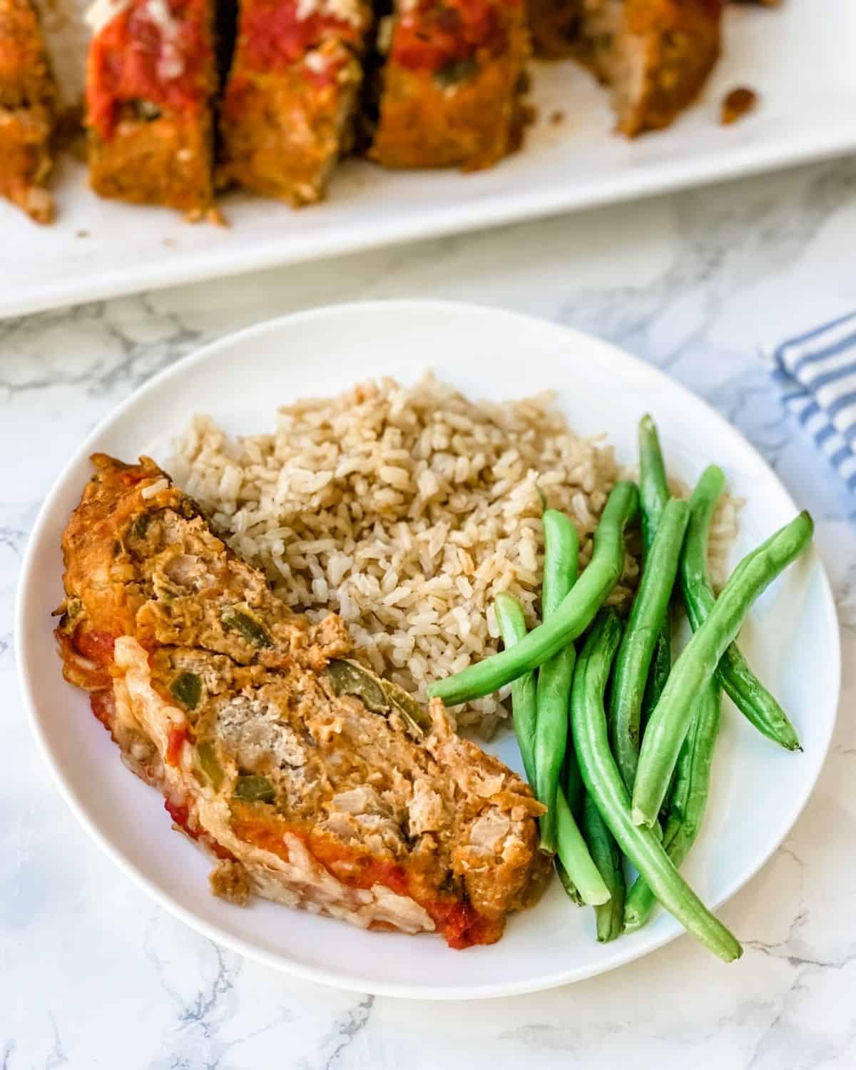 Sausage meatloaf on a plate with green beans and rice.
