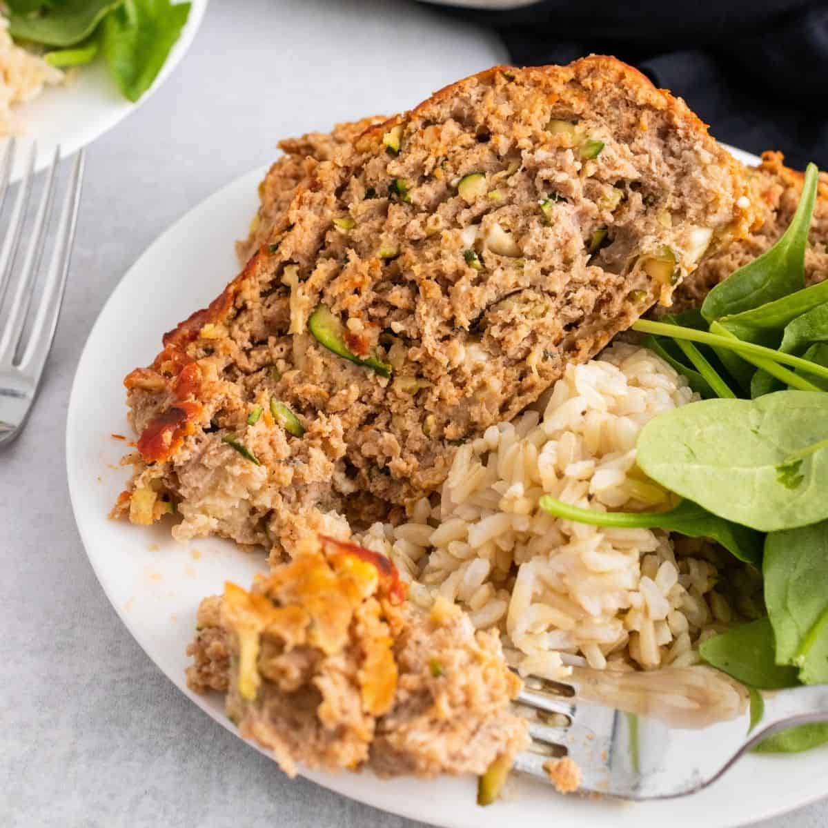 turkey zucchini meatloaf on a plate with rice and spinach.