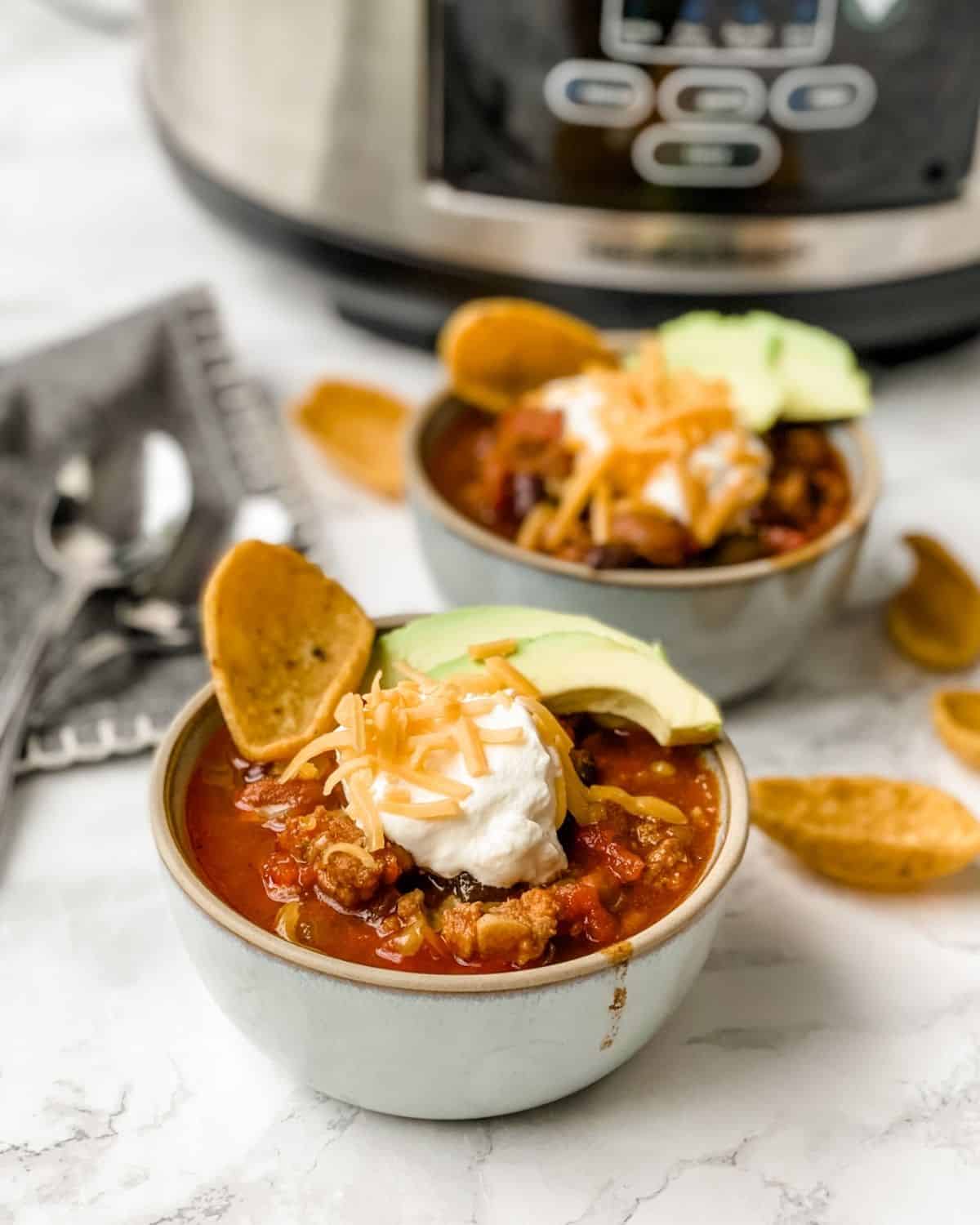two bowls of slow cooker sausage chili in front of a crockpot.