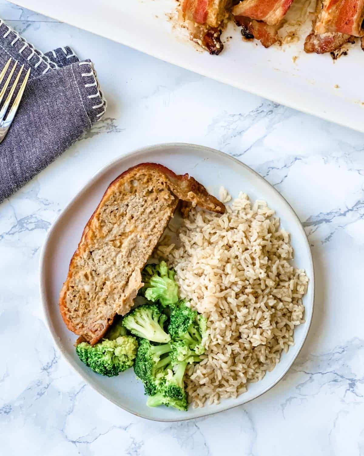 overhead picture of cheeseburger meatloaf on a plate with rice and broccoli.