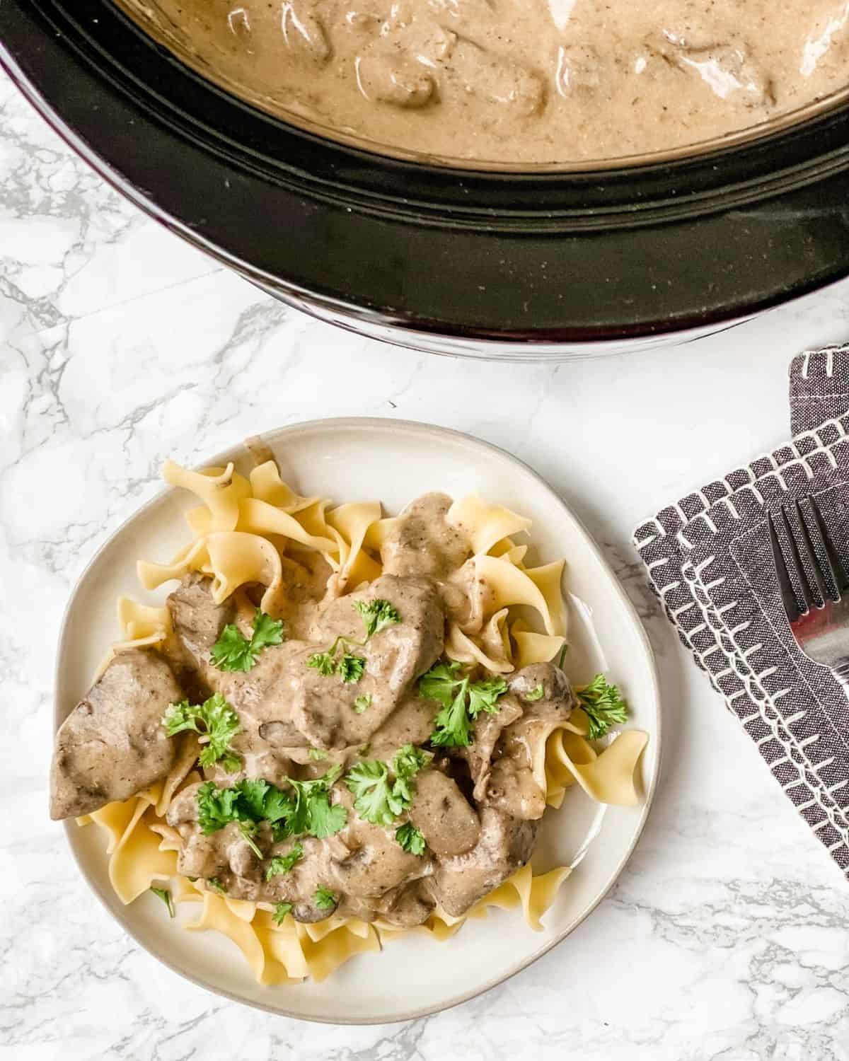 overhead picture of slow cooker beef stroganoff on a plate next to the slow cooker