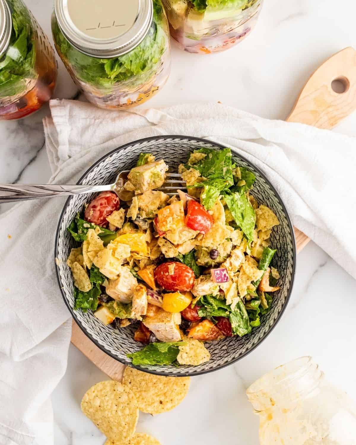 overhead picture of southwest chicken salad in a bowl with jars of salad behind it.