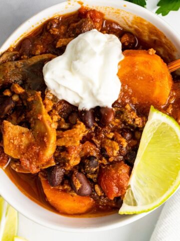 Overhead picture of turkey veggie chili in a white bowl. There's a piece of line and sour cream on top of the chili