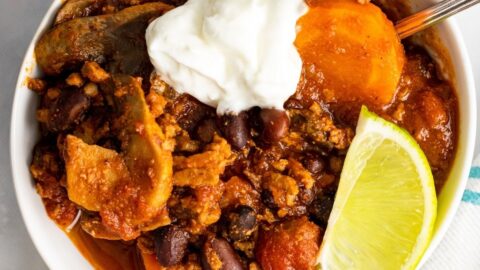 Overhead picture of turkey veggie chili in a white bowl. There's a piece of line and sour cream on top of the chili