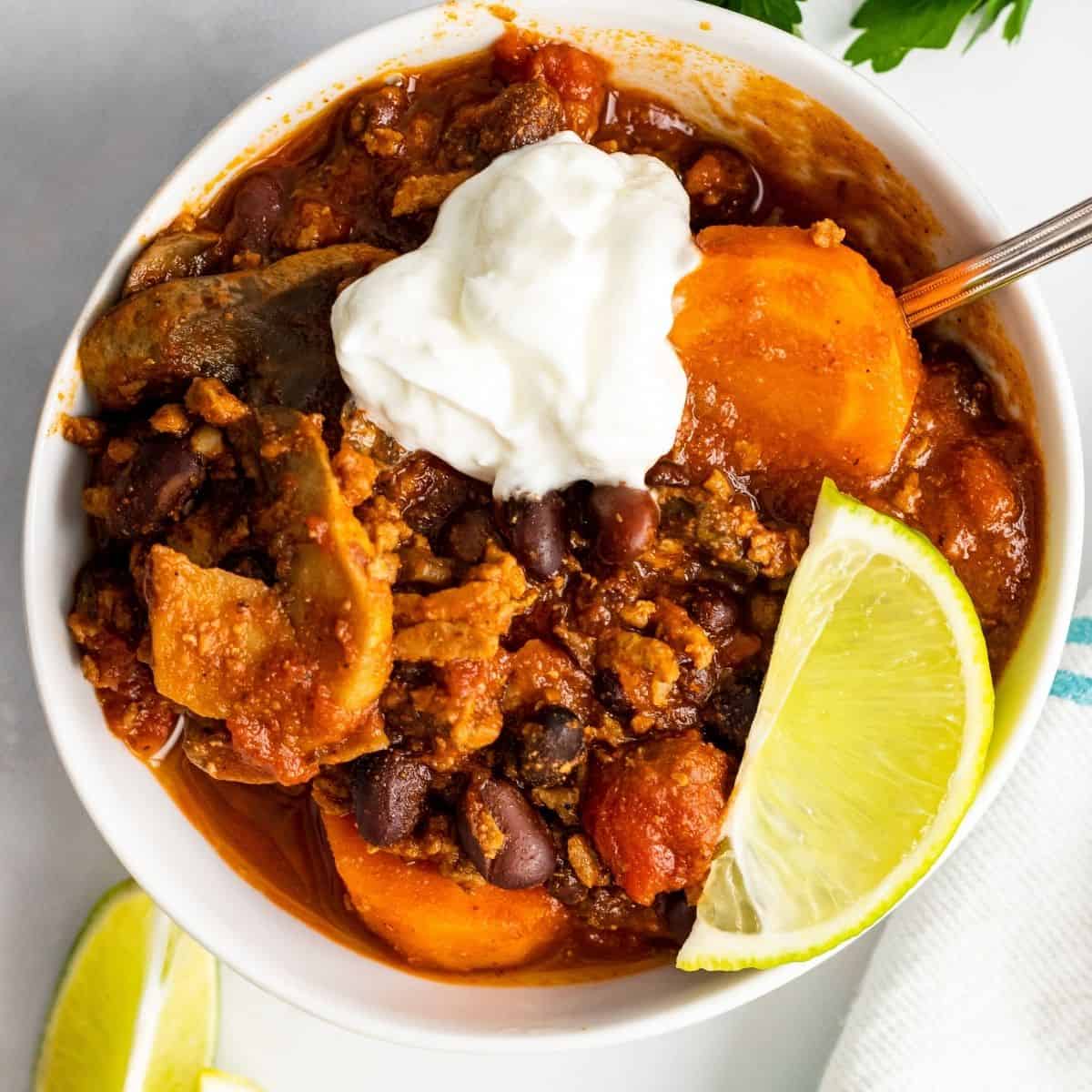 Overhead picture of turkey veggie chili in a white bowl. There's a piece of line and sour cream on top of the chili