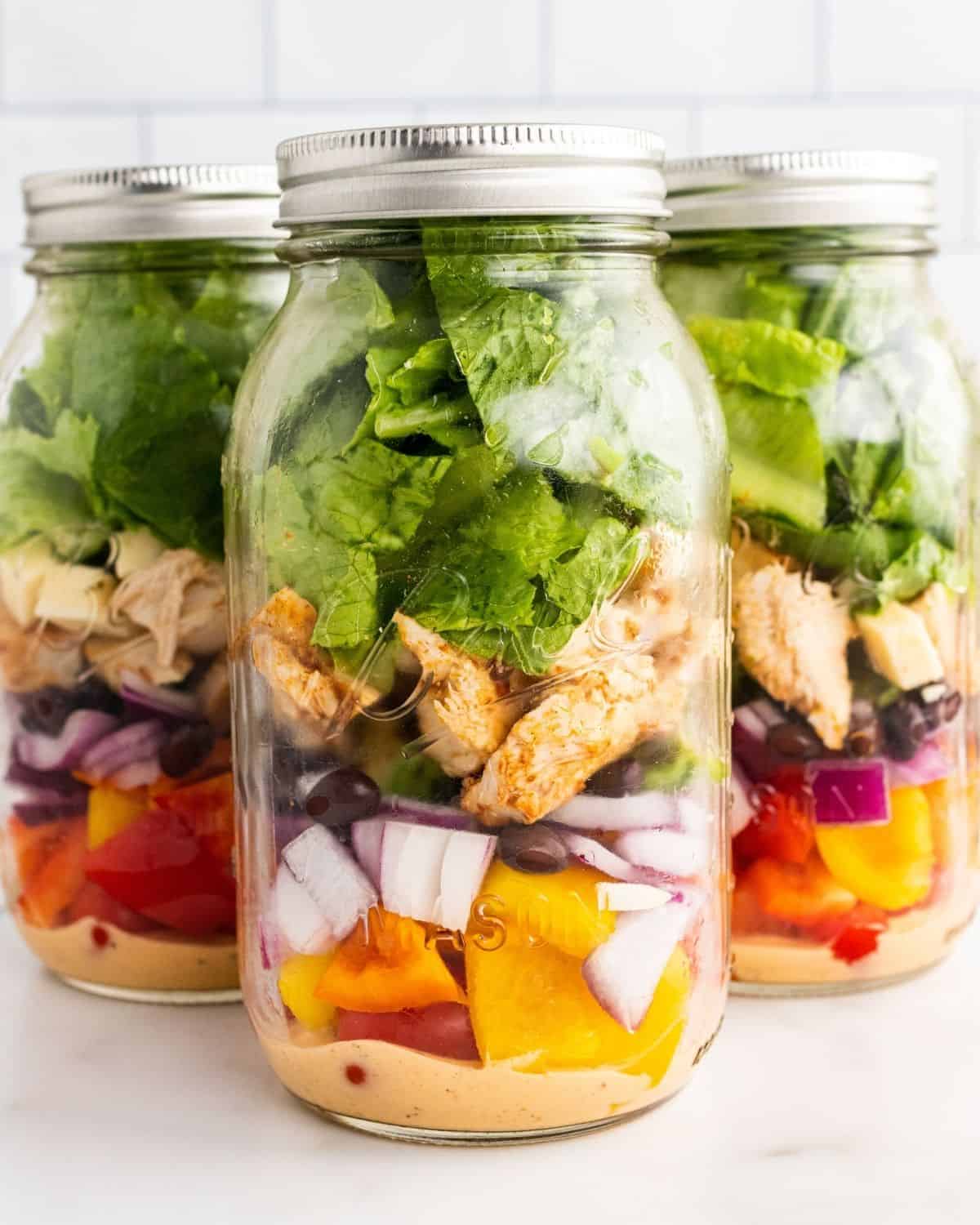5 mason jars layered with the ingredients for southwest chicken salad.