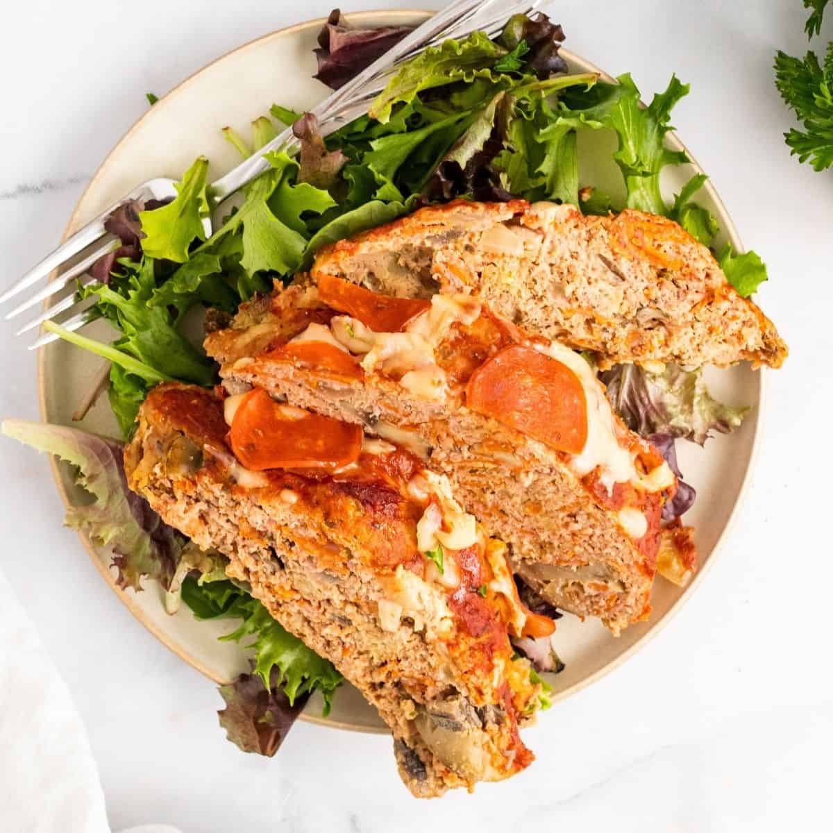 Three pieces of pizza meatloaf on a plate with spring greens and a fork.