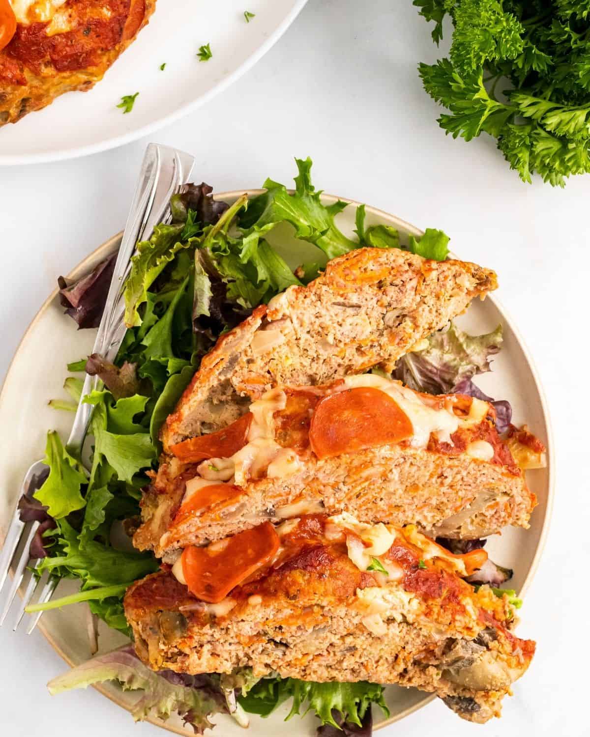 three slices of pizza meatloaf on a plate with salad greens