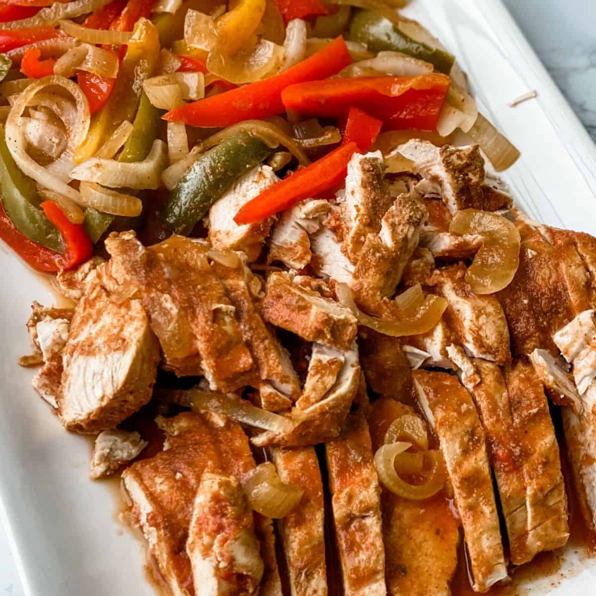 strips of chicken fajitas on a plate next to the onions and peppers.