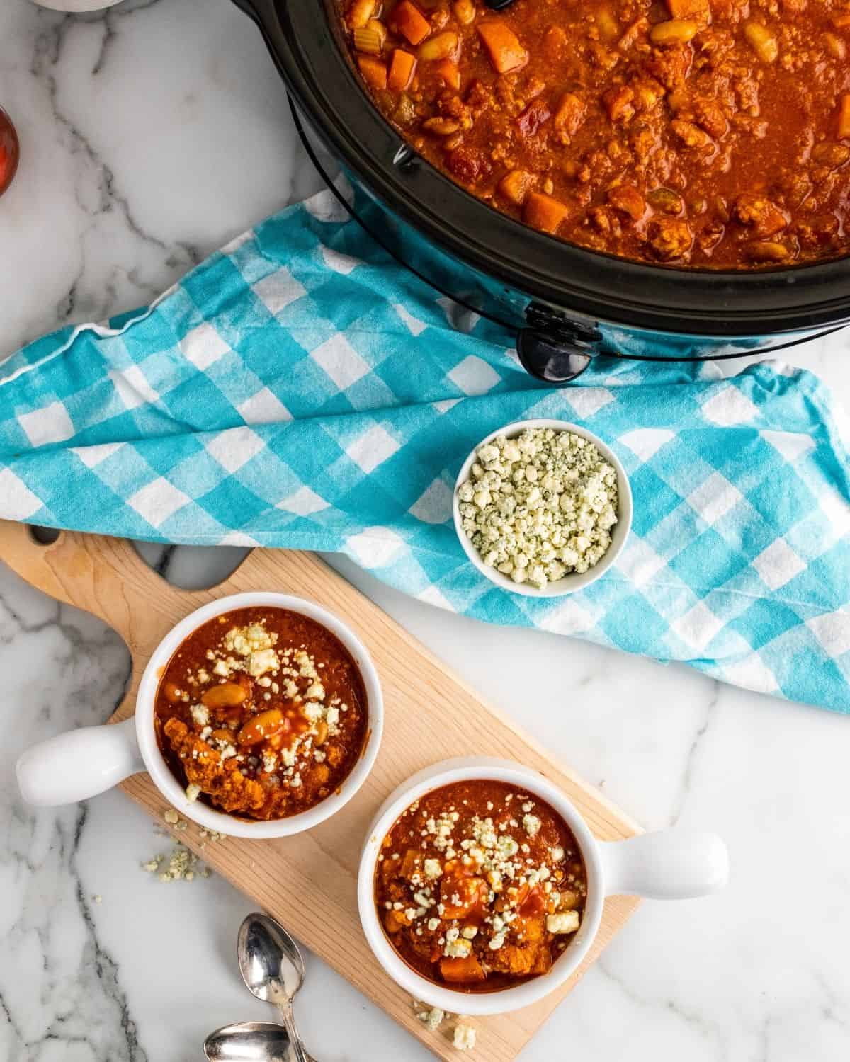 Two bowls of buffalo chicken chili next to a saucepan