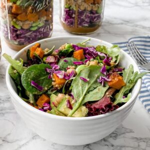 Spicy Thai salad in a jar.In a bowl with layered salad behind