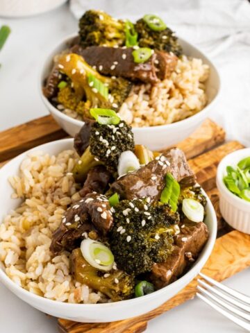 slow cooker beef and broccoli healthy recipe. Two bowls of beef broccoli on a cutting board.
