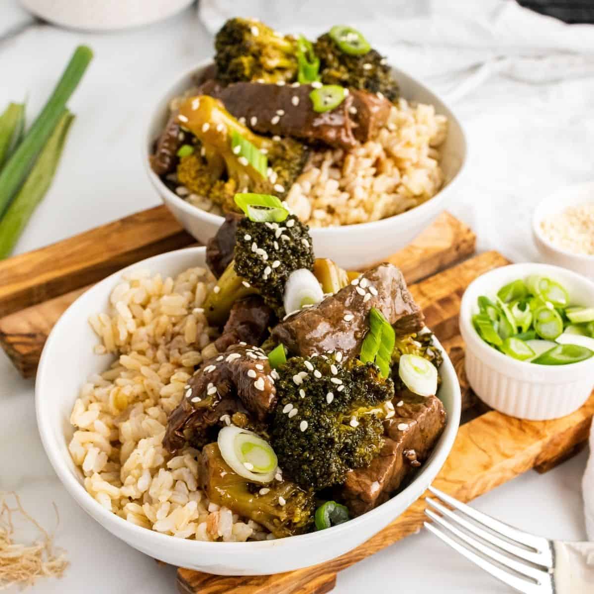 Slow Cooker Beef and Broccoli Healthy recipe in the crockpot. Two bowls on a cutting board with rice and beef broccoli.
