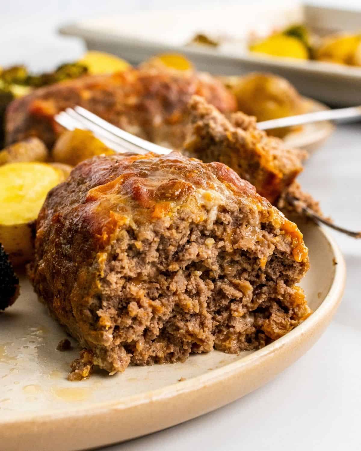 close up of a small meatloaf cut in half on a plate with potatoes.