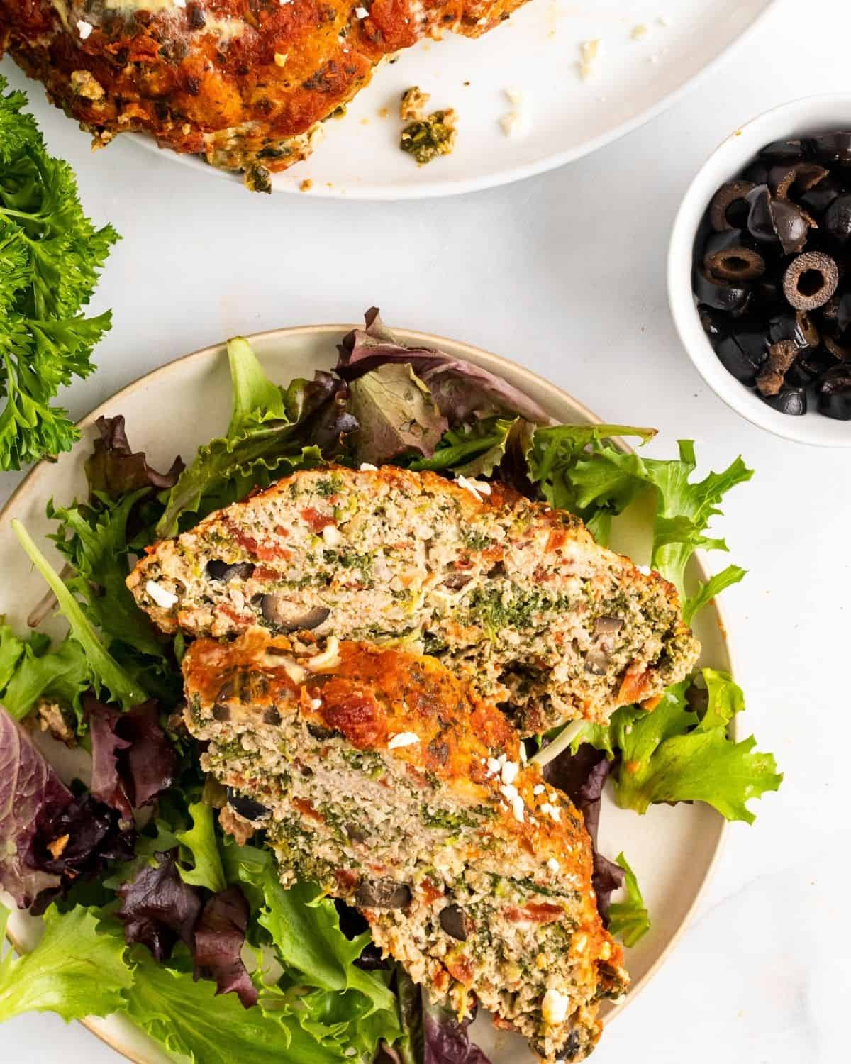 two slices of greek meatloaf on a plate with field greens