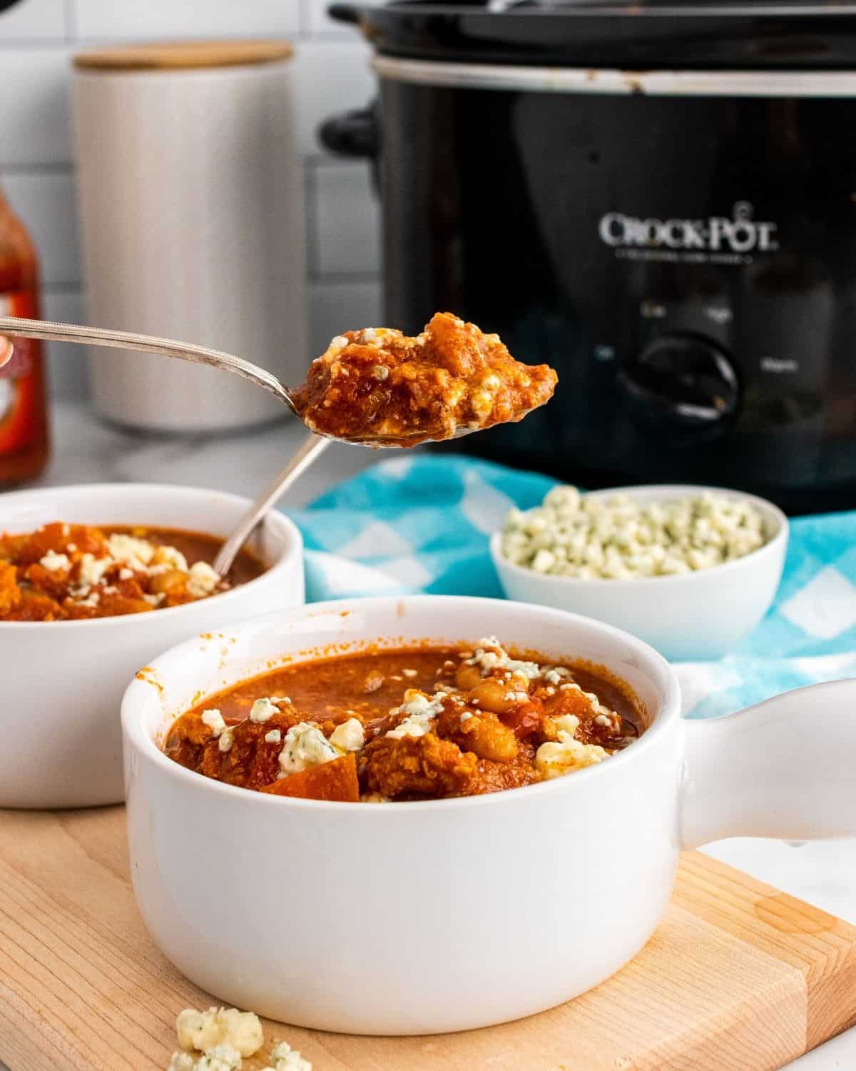 Closeup photo of buffalo chicken chili in a bowl with a scoop of chili baby in a crockpot.