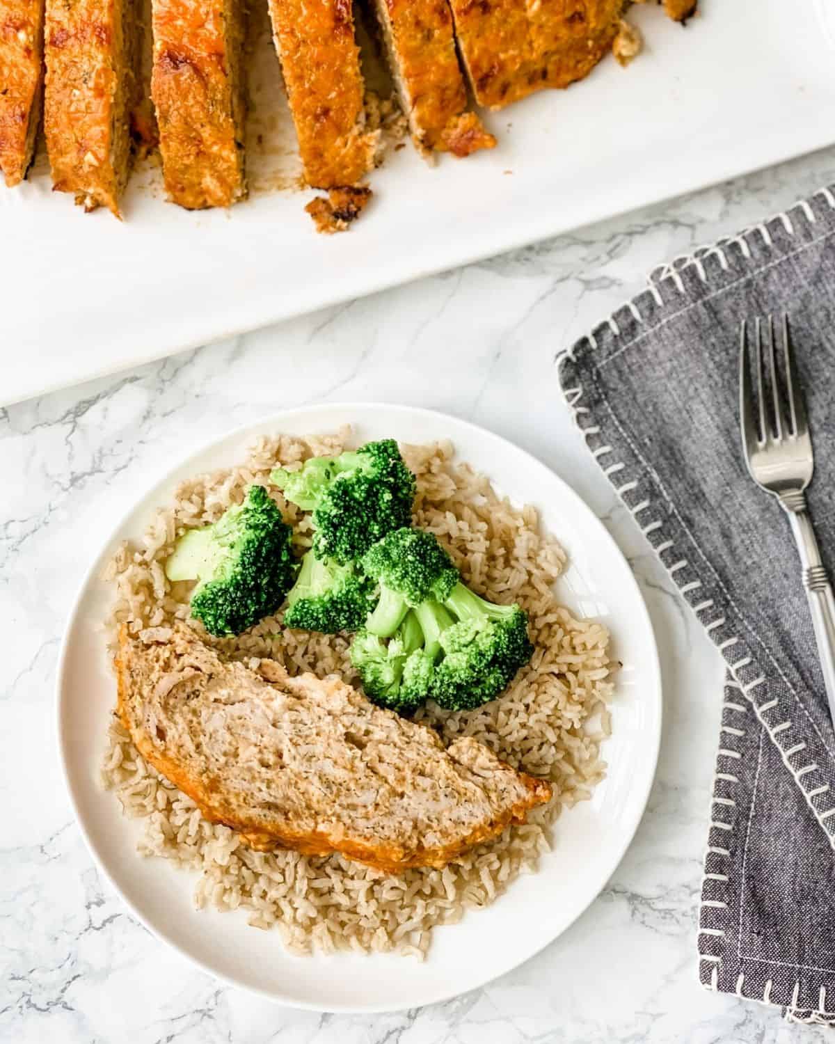 a slice of buffalo chicken meatloaf on plate next to a platter with sliced meatloaf.