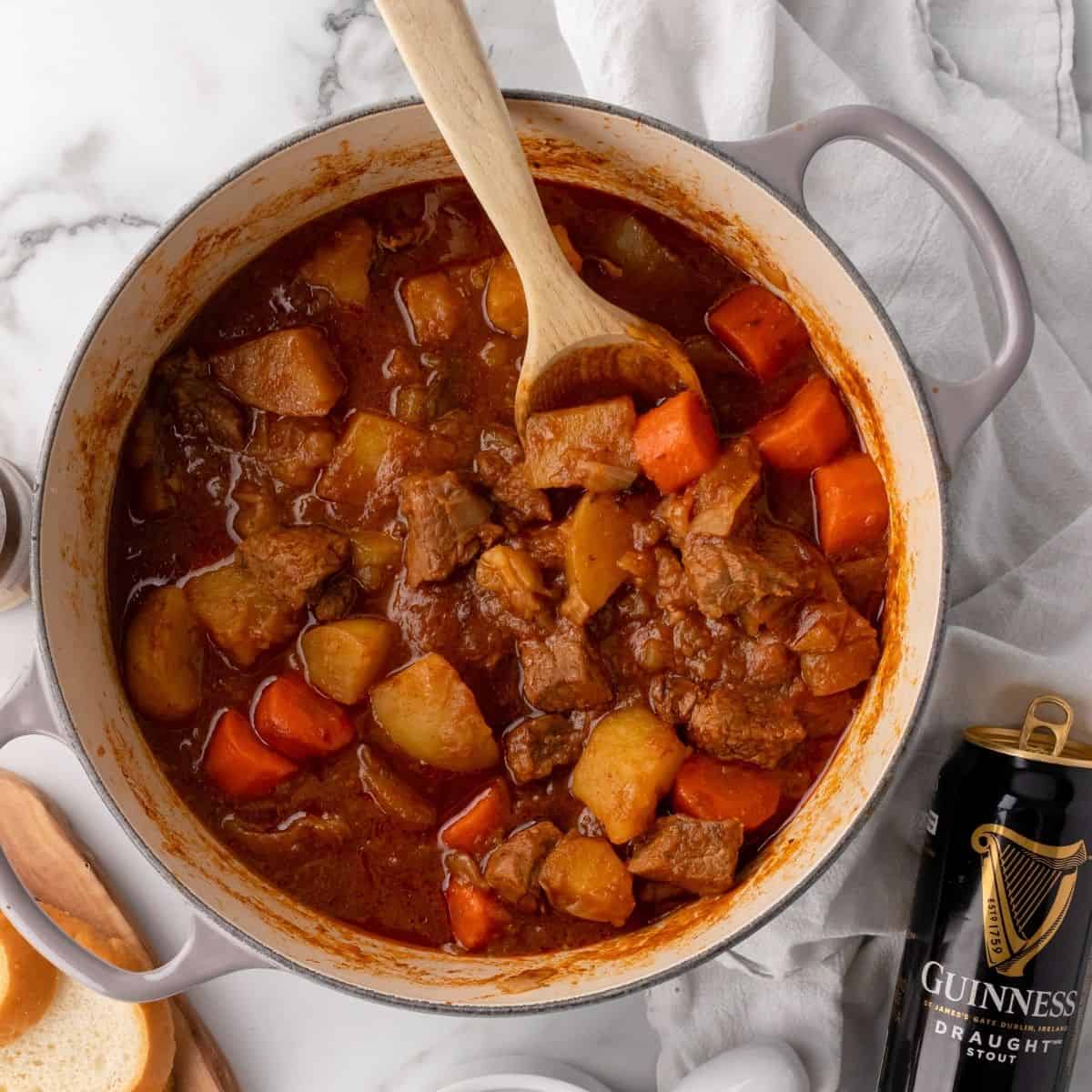 Guinness beef stew in a soup pot with a spoon and a can of Guinness stout next to it.