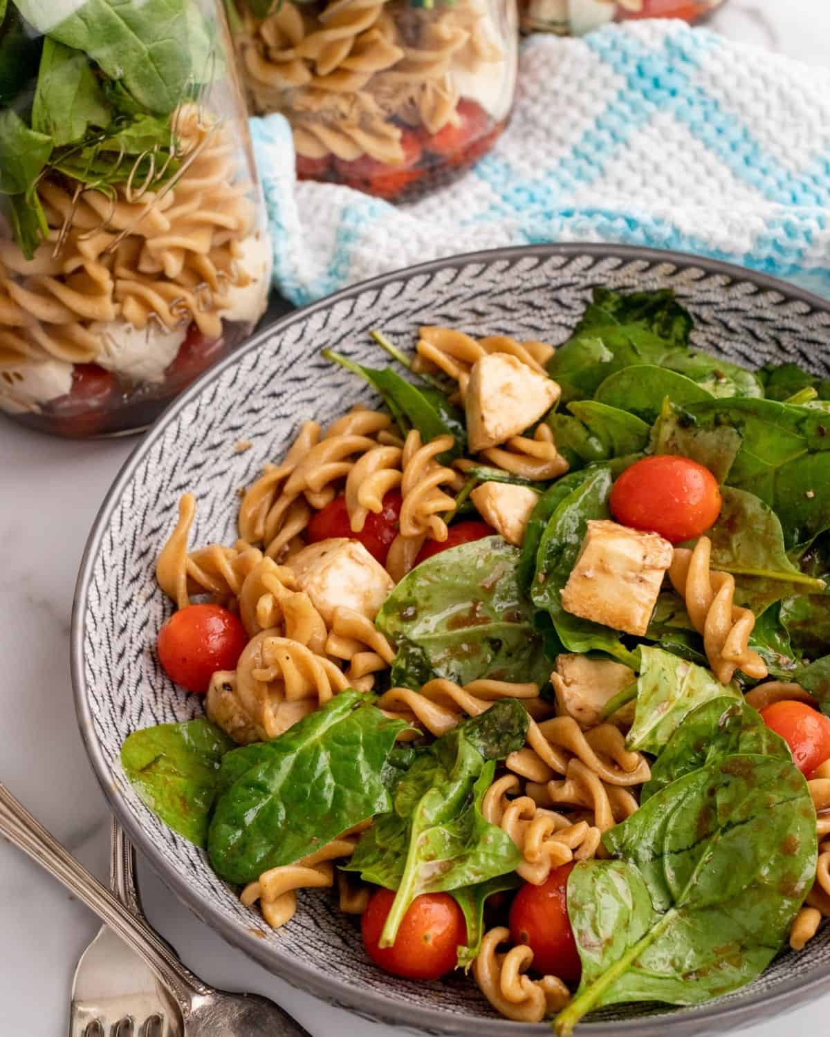 spinach pasta salad with pieces of fresh mozzarella and tomatoes.