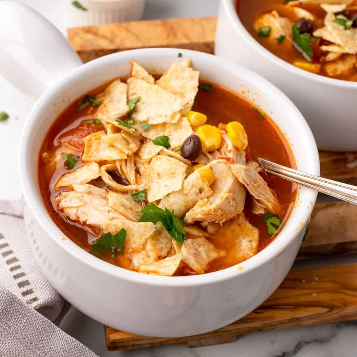 easy chicken tortilla soup in a white bowl with a spoon.