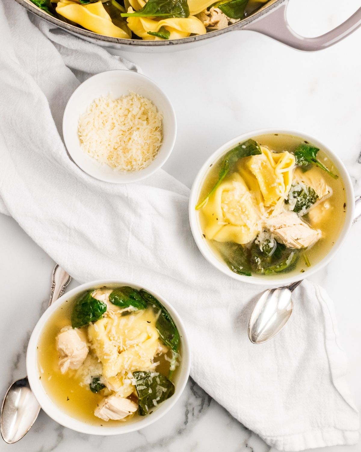 overhead picture of two bowls of chicken tortellini with spinach with grated cheese in a bowl next to it