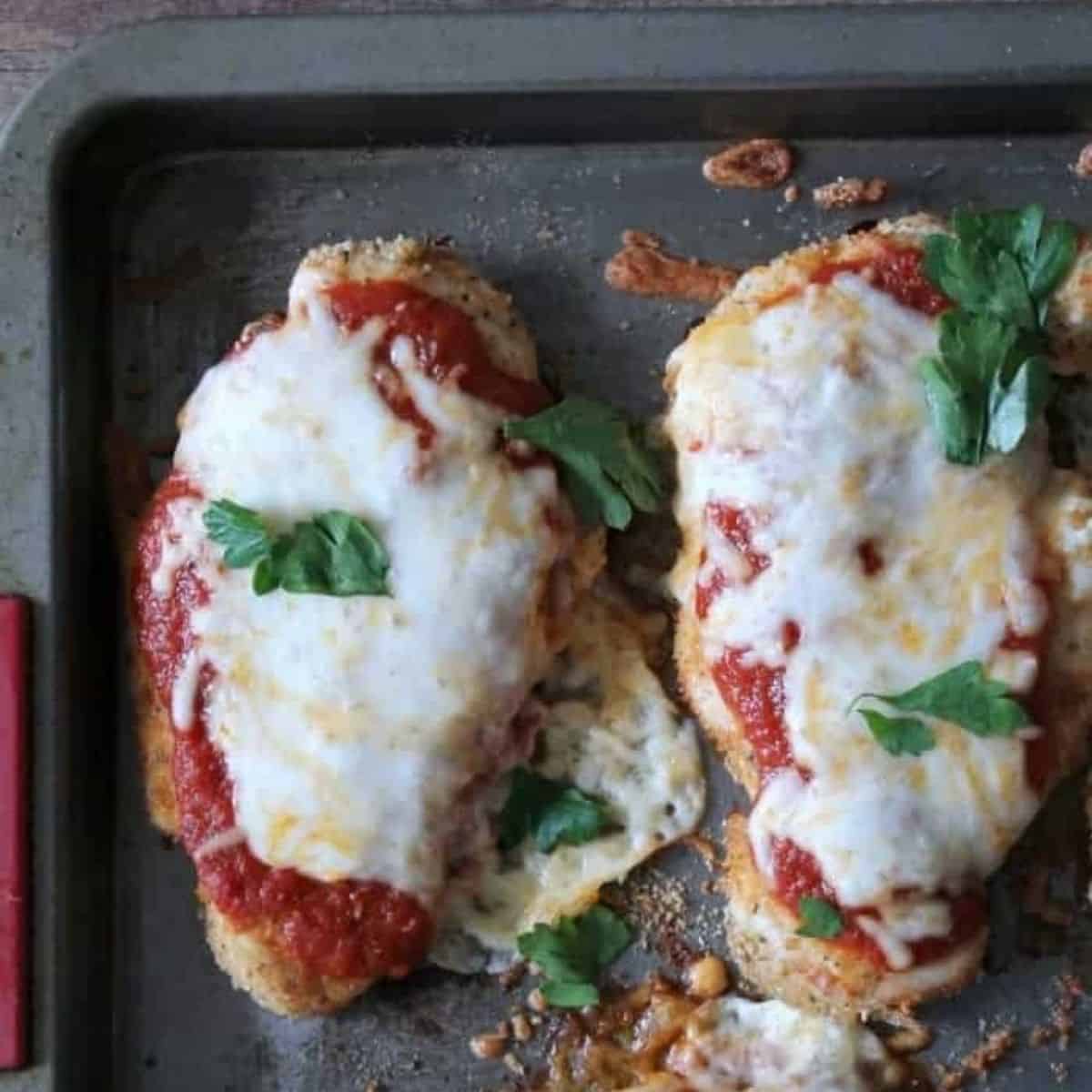 baked Chicken Parmesan on a sheet pan with sauce and cheese.