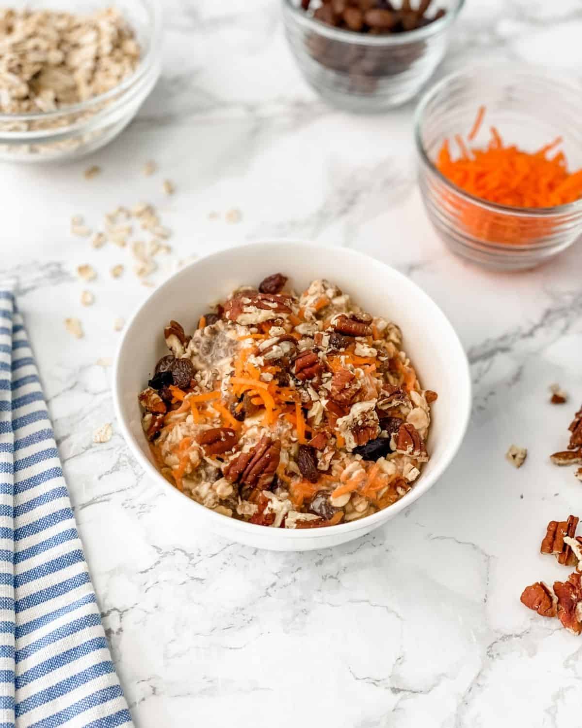 picture of carrot cake overnight oats with shredded carrots, pecans, and oats around the bowl.