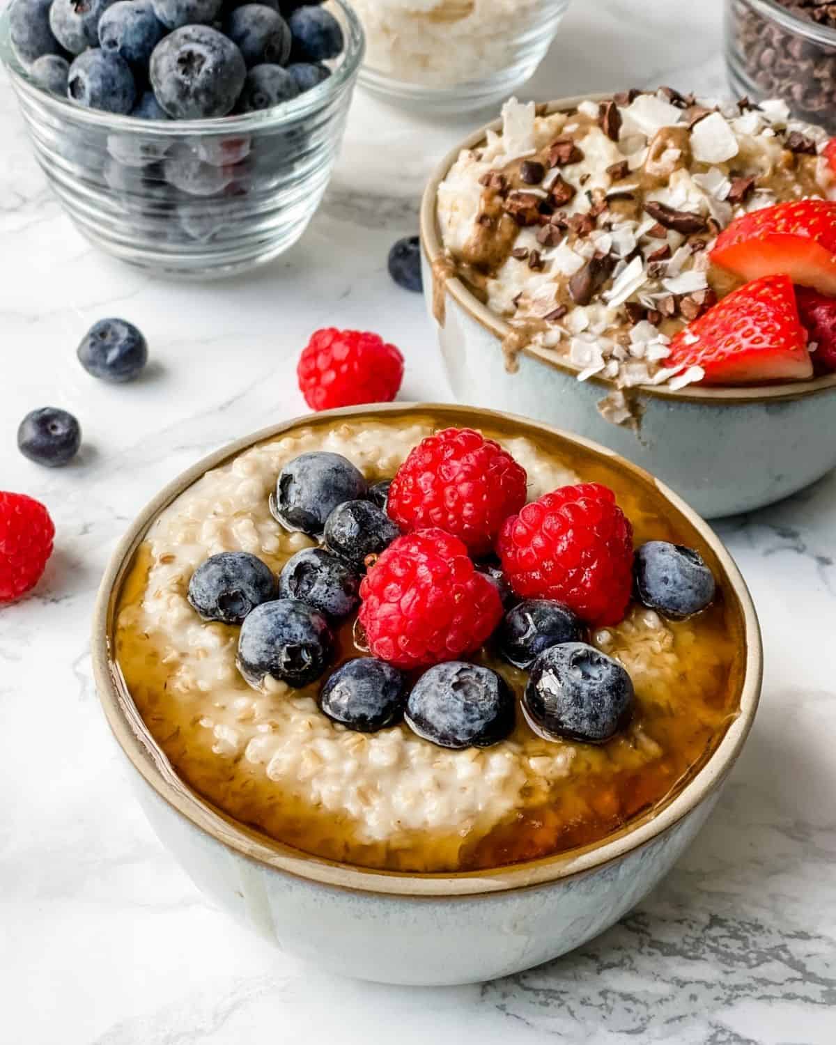 two bowls of oatmeal with toppings. One has berries and the other one with coconut and cacao nibs.