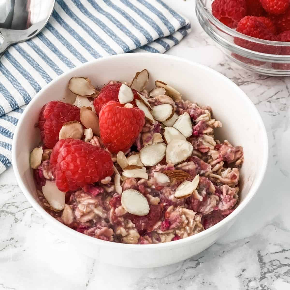 a bowl of raspberry overnight oats with sliced almonds and raspberries on top.