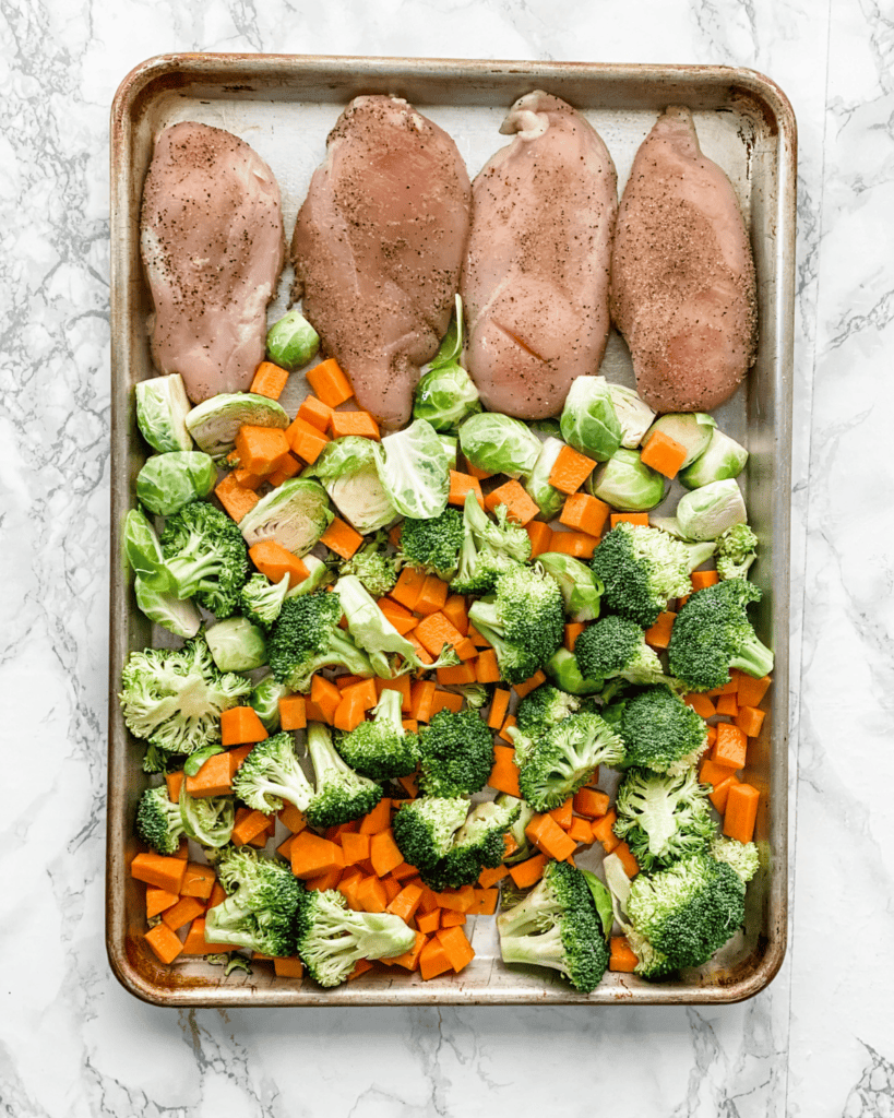 raw chicken and vegetables on a sheet pan.