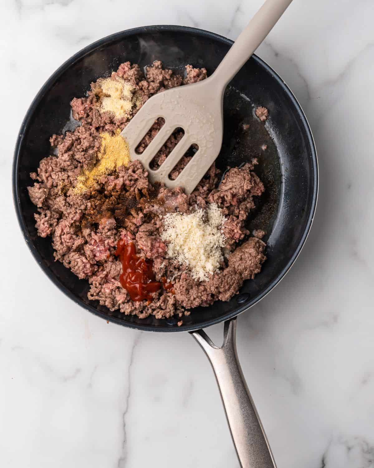 ground beef cooking in a skillet with mustard and ketchup.
