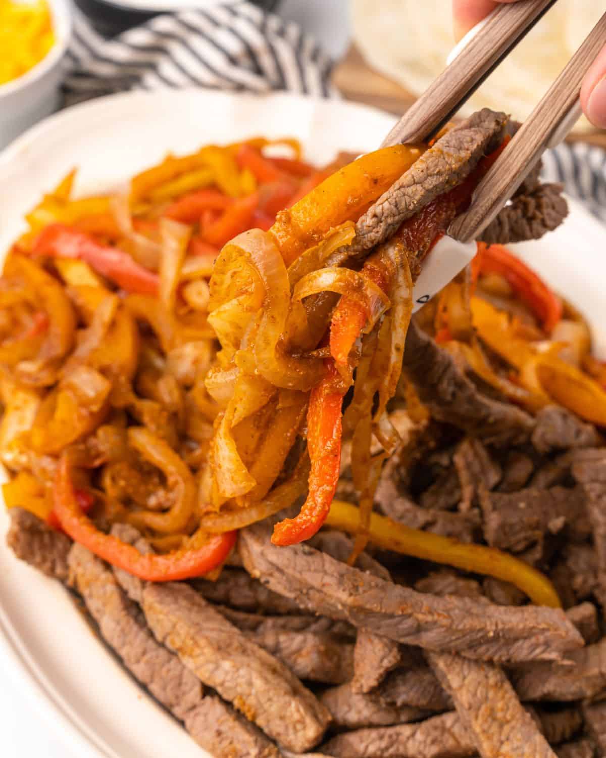 close up picture of someone picking up the steak and peppers with tongs.