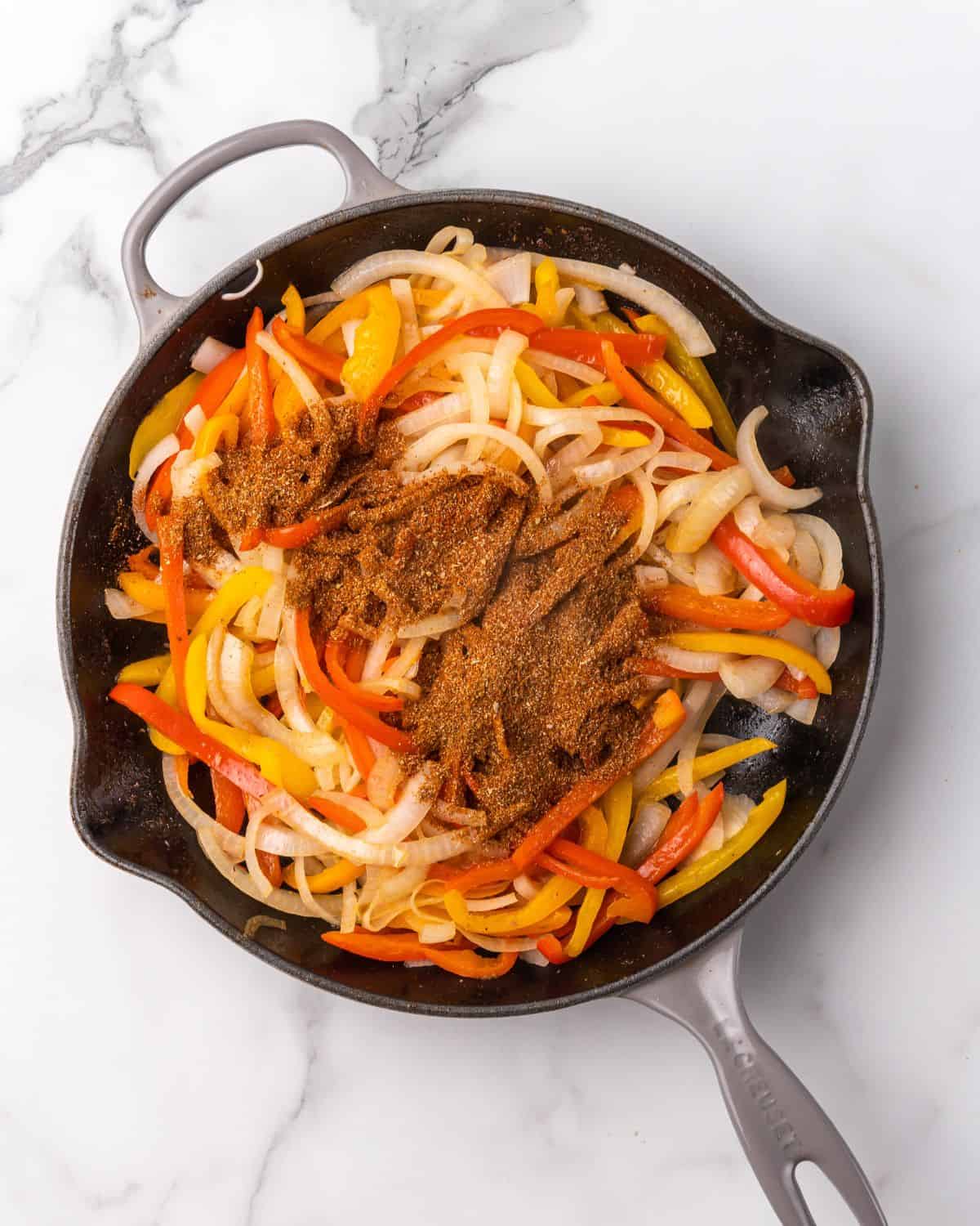 onions and peppers cooked in a skillet with fajita seasoning on top.
