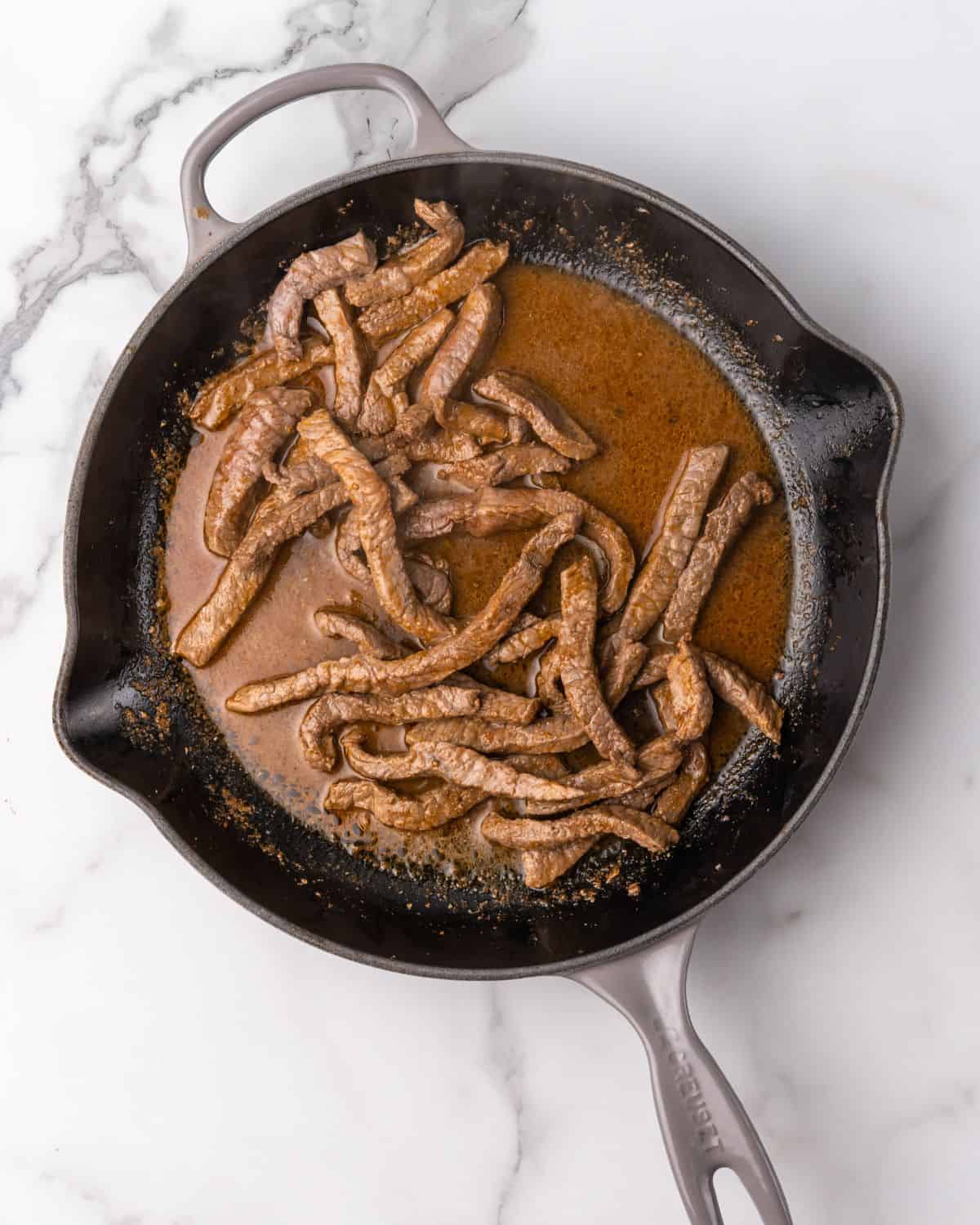 steak strips with fajita seasoning and water in a skillet.