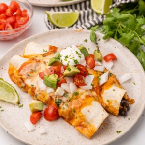 two enchiladas on a plate with sauce and sour cream.